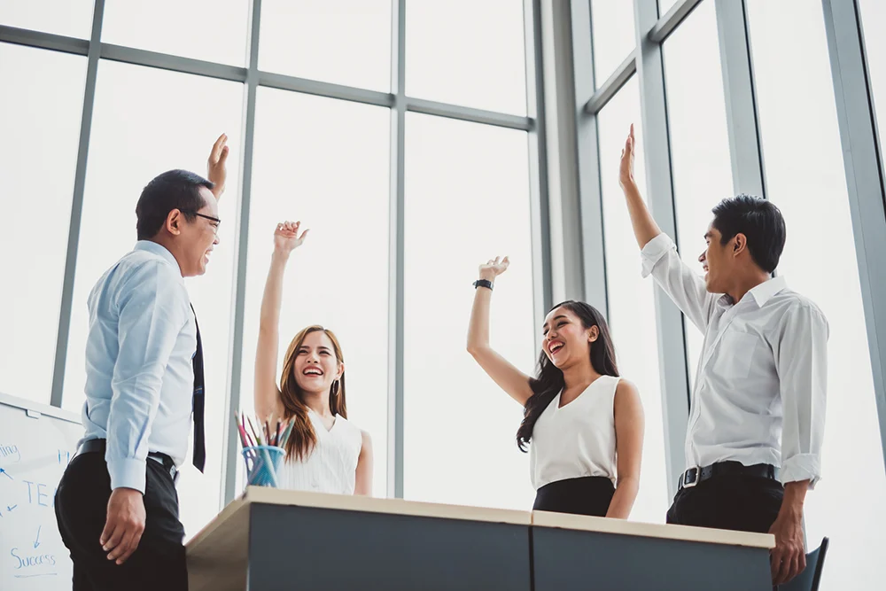 A group of professionals in a team meeting, raising their hands