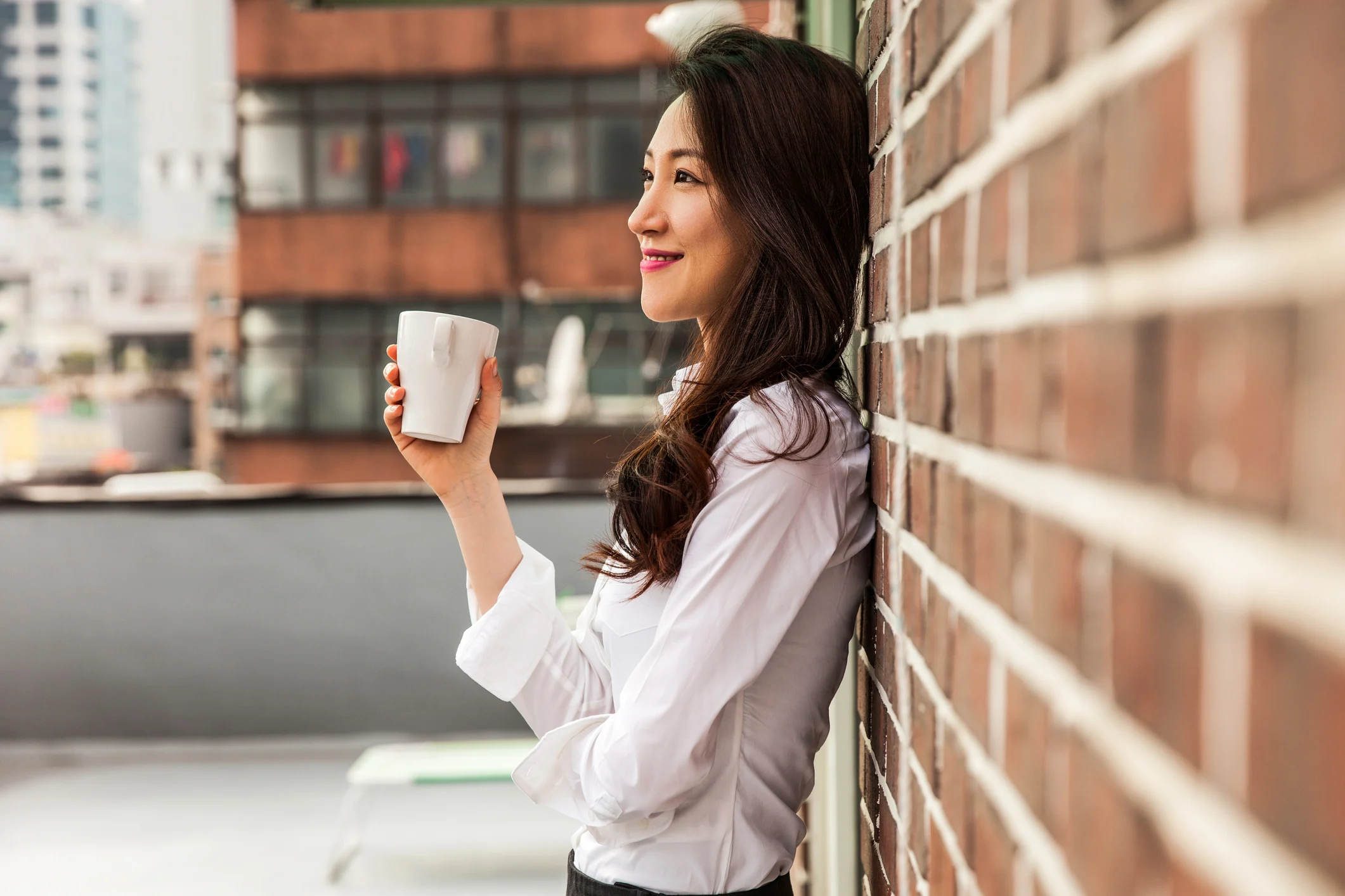 woman leaning against brickwall holding cup of coffee - volunteering article