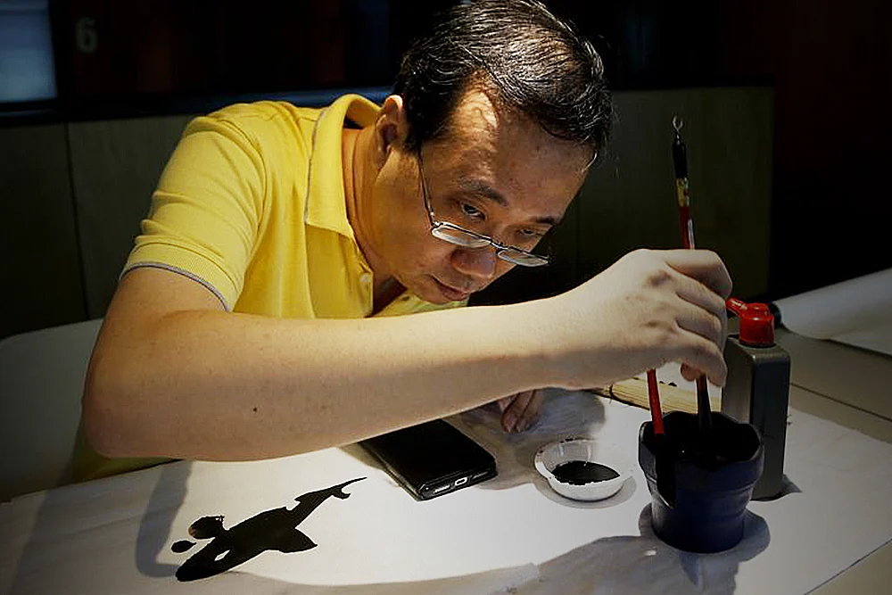 Wesley seah doing Chinese painting, employee discussing project ideas with team at desk