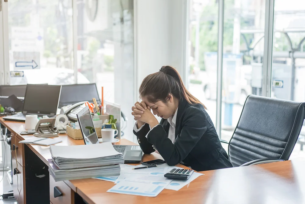 woman stressed with piles of paper on her table