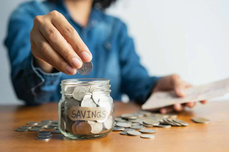 Close-up of a person saving coins in a jar at a desk