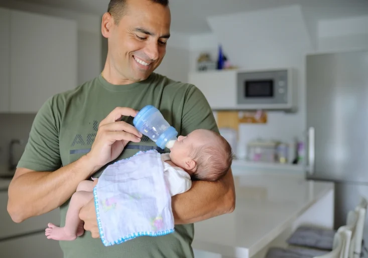a dad feeding his baby with milk in his arms