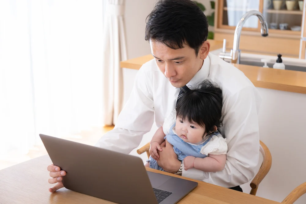 A father holding his baby in his lap while working remotely from home