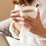 girl holding a cup of coffee while looking at a laptop screen