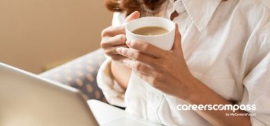 girl holding a cup of coffee while looking at a laptop screen