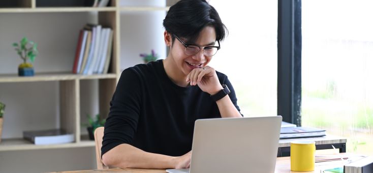 young asian smiling while looking at laptop screen