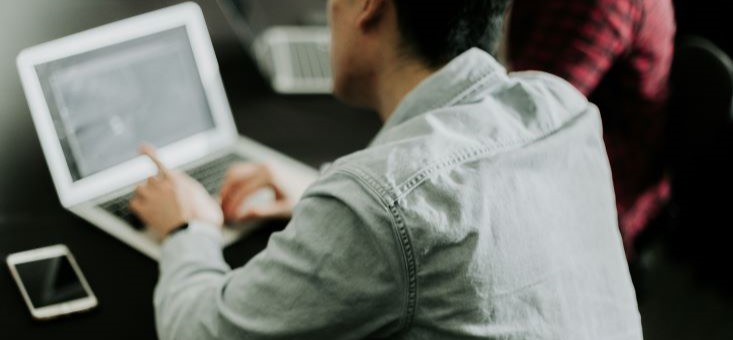 A man seated at a desk, focused at work on his laptop