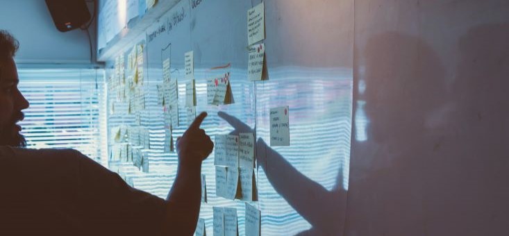 A man points at a whiteboard filled with sticky notes.