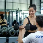 Career health is likened to physical health as seen in this image depicting a female gym instructor teaching a man how to lift weights