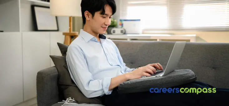Asian Chinese man sitting on couch working on laptop on lap